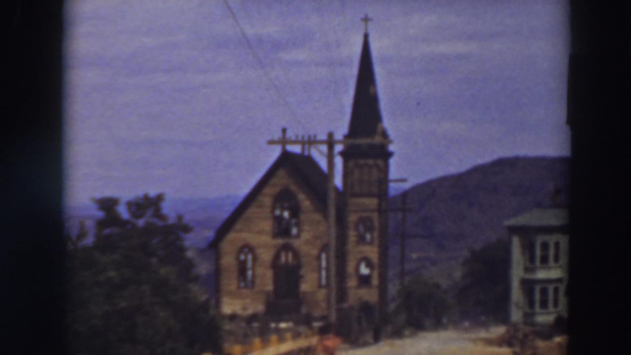 Small steepled church beside utility poles with mountains in the background.