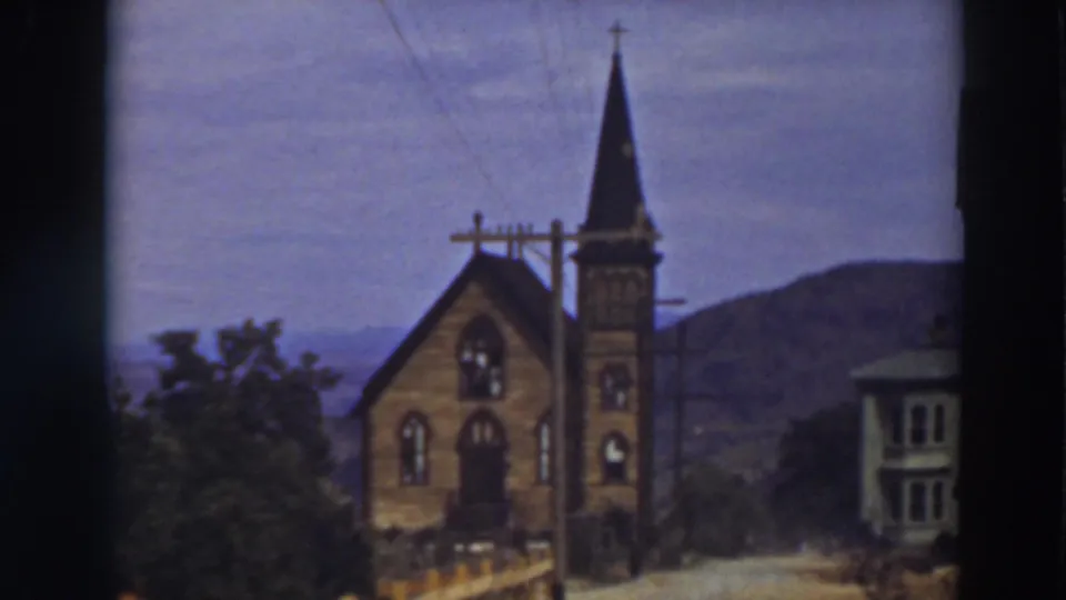 Small church exterior in the stated Virginia City setting, with a neighboring house, power lines, trees, and distant hills visible.