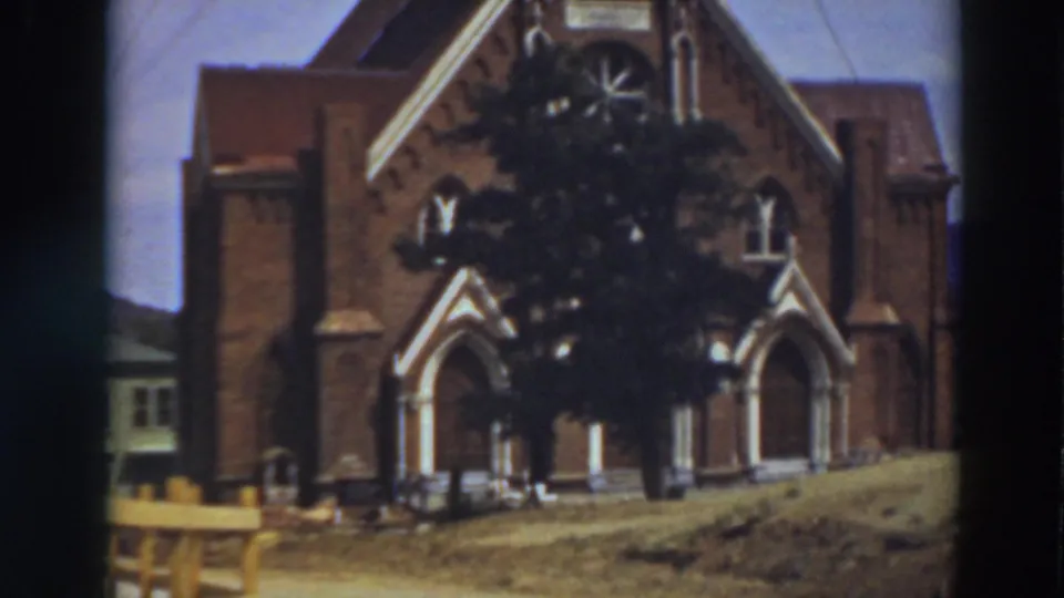 1937 8mm view of St. Mary's Cathedral in Virginia City, California, showing arched entrances, brickwork, and a tree across the facade.