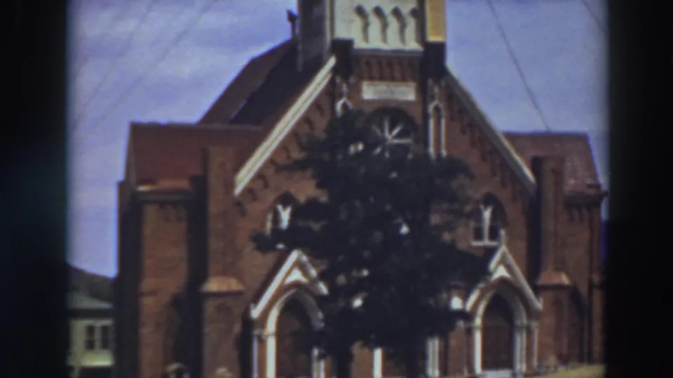 1937 8mm frame of St. Mary's Cathedral showing more of the upper facade, roofline, arched entries, and tree in front.