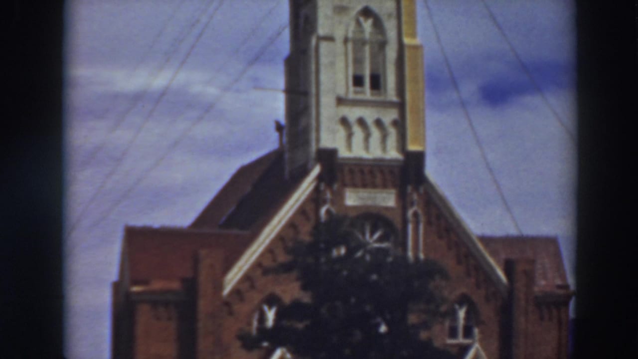 1937 Virginia City, California 8mm frame showing a church facade, tower base, arched openings, overhead wires, and cloudy sky.
