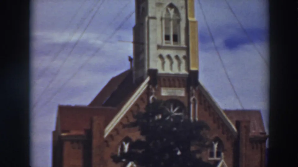 1937 Virginia City, California 8mm frame showing a church facade, tower base, arched openings, overhead wires, and cloudy sky.