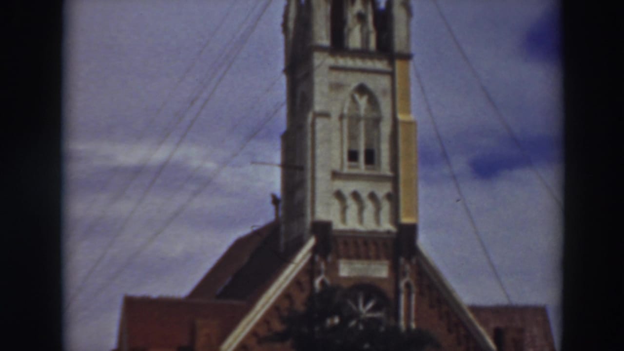 Church steeple and roofline framed by dark film borders and overhead wires.