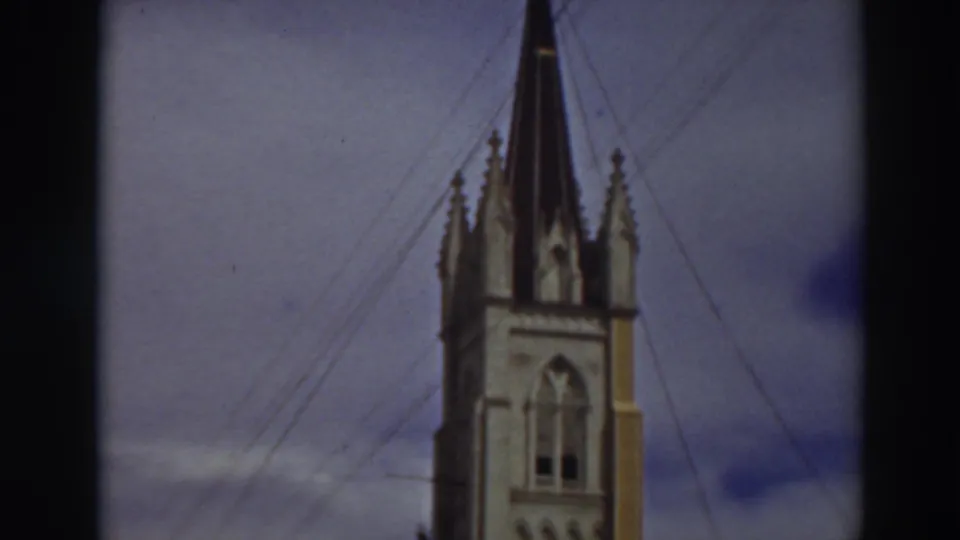1937 Virginia City, California frame showing the upper church steeple, cross, spired corners, guy-wires, and cloudy sky.