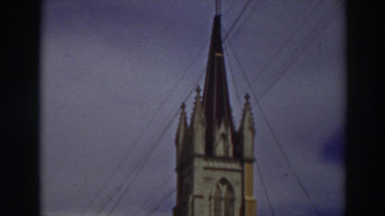 Ornate white building with a tall spire and a yellow car parked along the street.