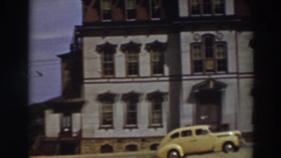 A 1937 home-movie frame shows a yellow period car outside an ornate white building in Virginia City, California.