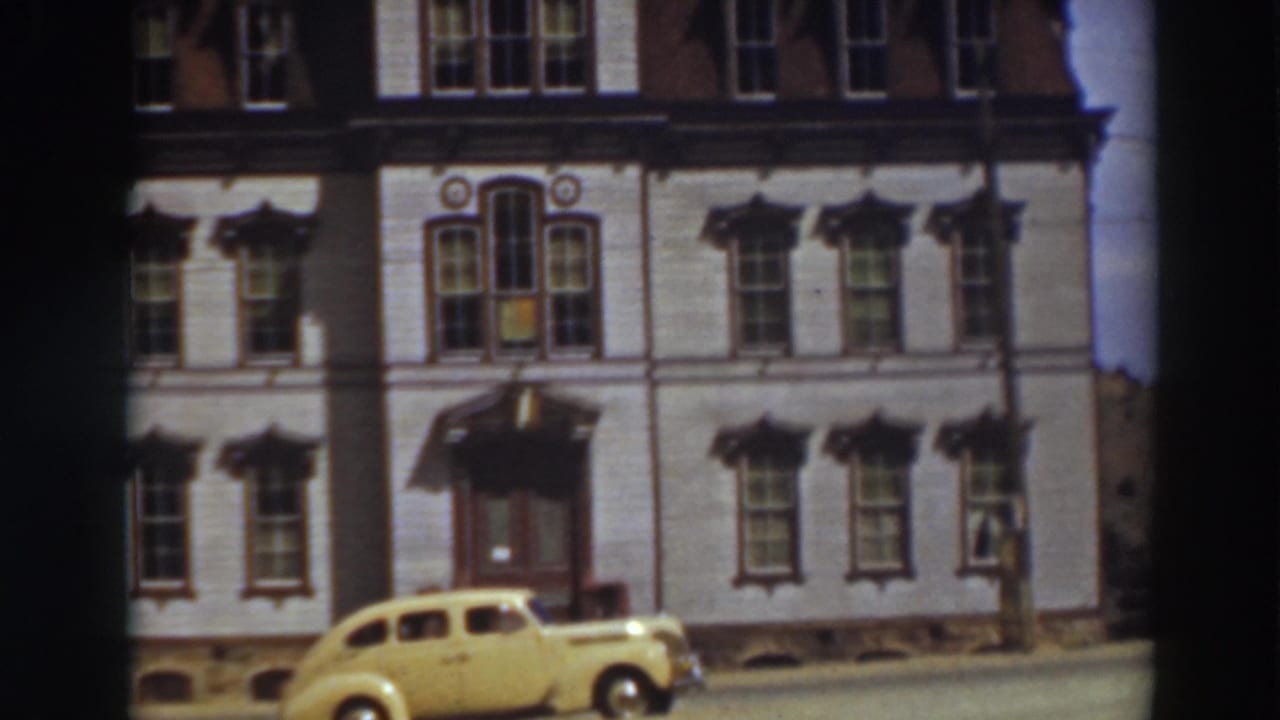 Yellow sedan parked before a pale multi-story building with tall windows.