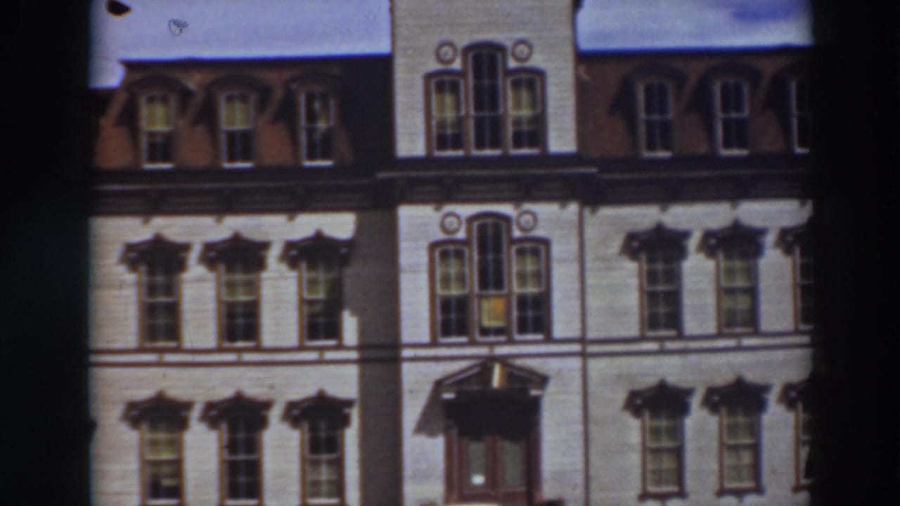 Upper facade of a pale building with ornate windows, roof dormers, and entrance canopy.