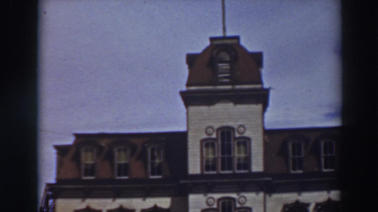 1937 8mm frame of the upper facade of Historic Bowers Mansion, showing red roof dormers, a central tower, and a flagpole.