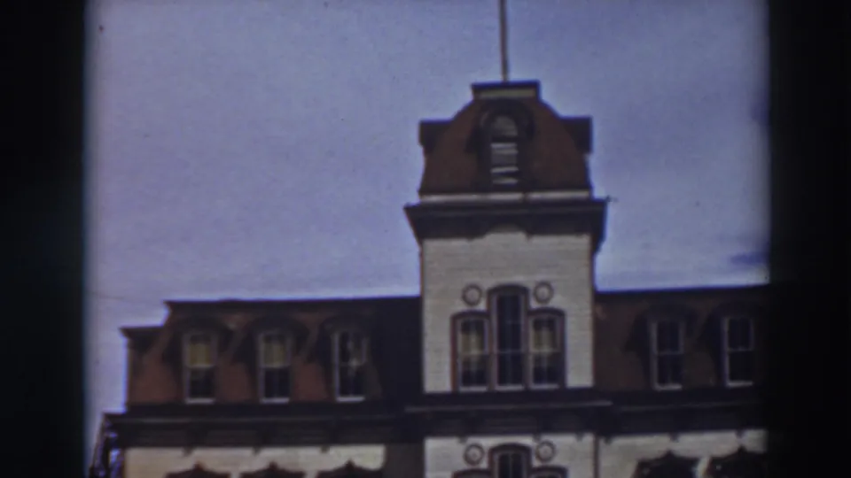 1937 8mm frame of the upper facade of Historic Bowers Mansion, showing red roof dormers, a central tower, and a flagpole.