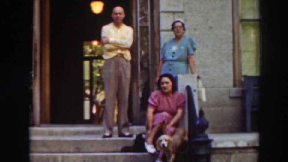 1937 8mm frame showing the porch group in Virginia City, California, with the seated woman turned slightly and the dog at her feet.