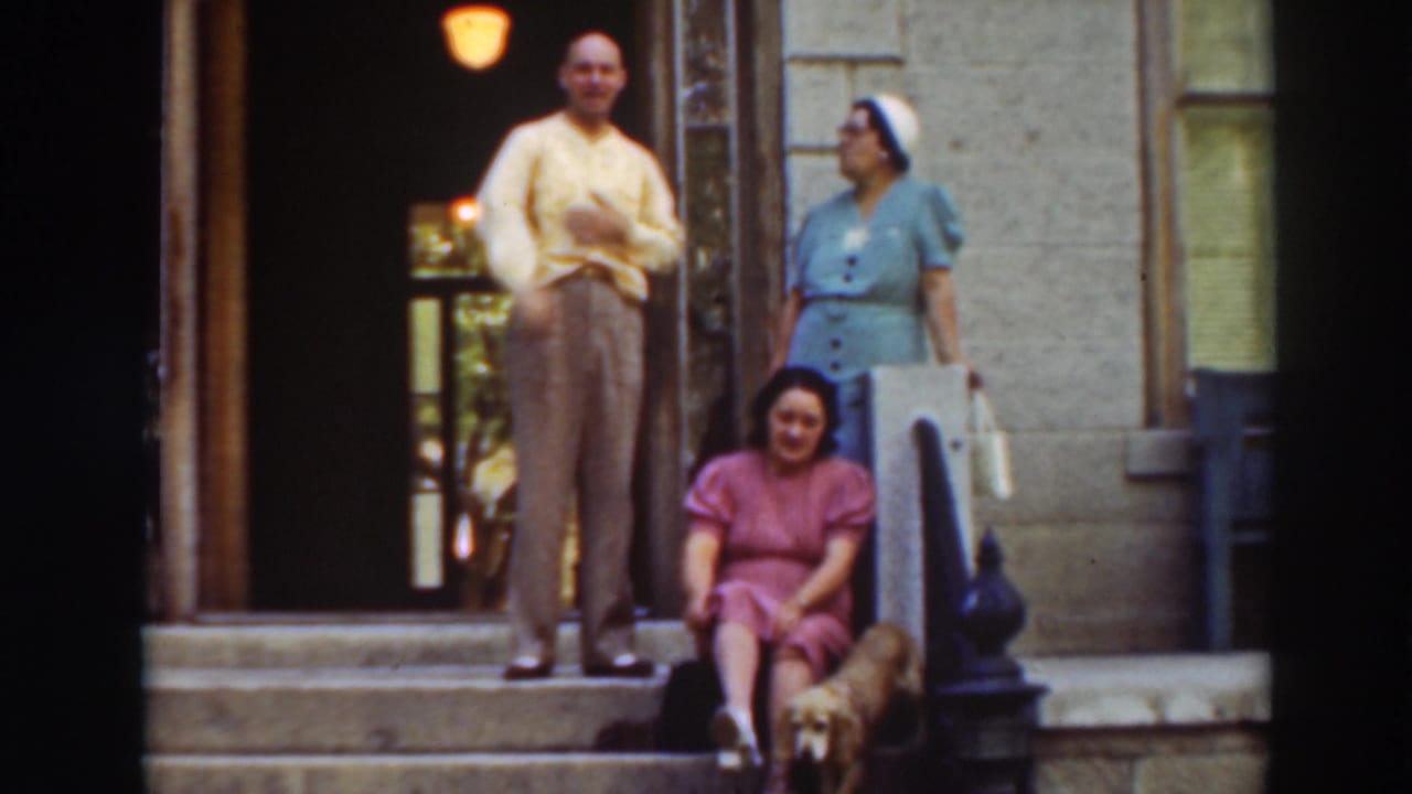 Three adults and a small dog posed on steps outside a large building entrance.