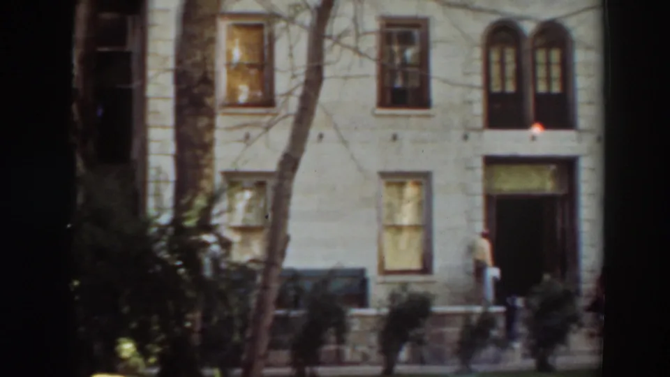 Wide 1937 frame of the building exterior in Virginia City, California, with arched windows, a doorway, trees, and a person near the entry.