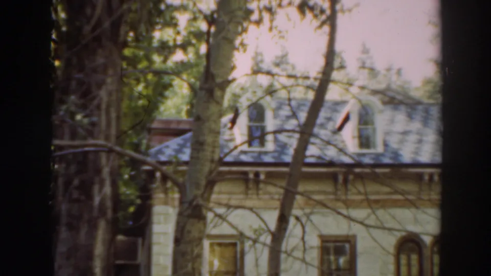 A closer 1937 home-movie view shows dormer windows, a pale upper facade, and trees crossing the house exterior.