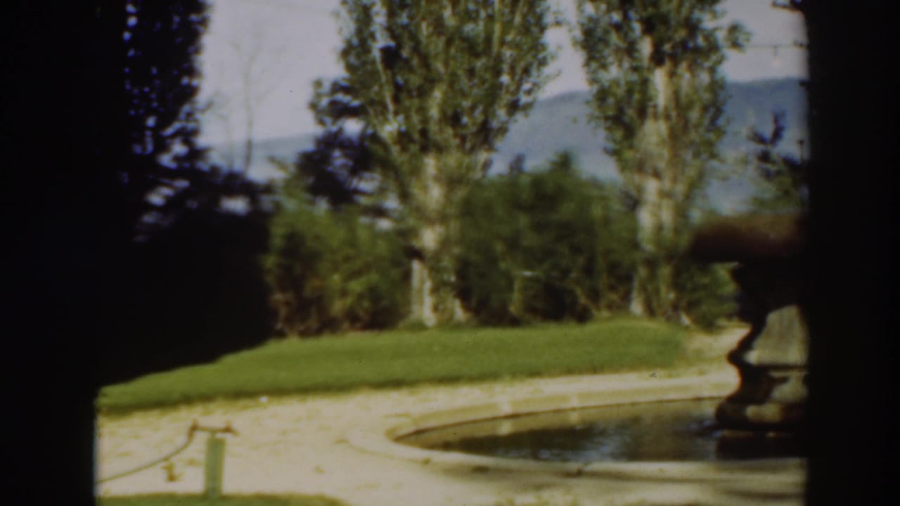 Circular garden fountain beside lawn, trees, and a distant hill.