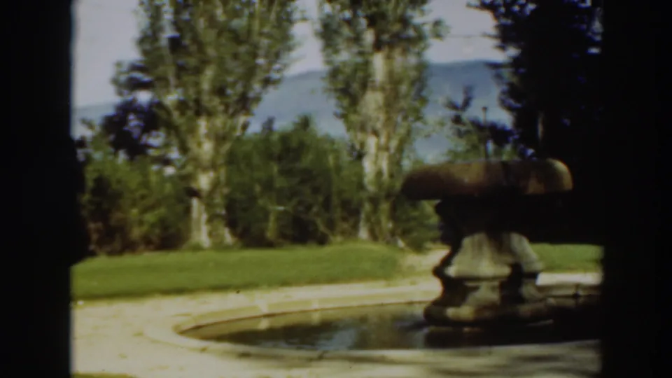 1937 8mm frame showing the fountain shifted right in the garden view, with lawn, trees, and hillside beyond.