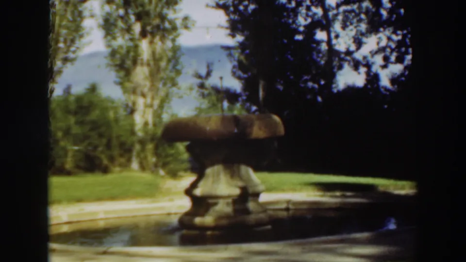 Late frame of the 1937 Virginia City garden clip, with the fountain in shade and trees and hillside beyond the lawn.