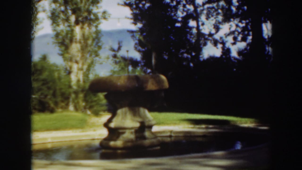 Yellow-toned stone fountain beside a reflection pool with trees and distant hills.