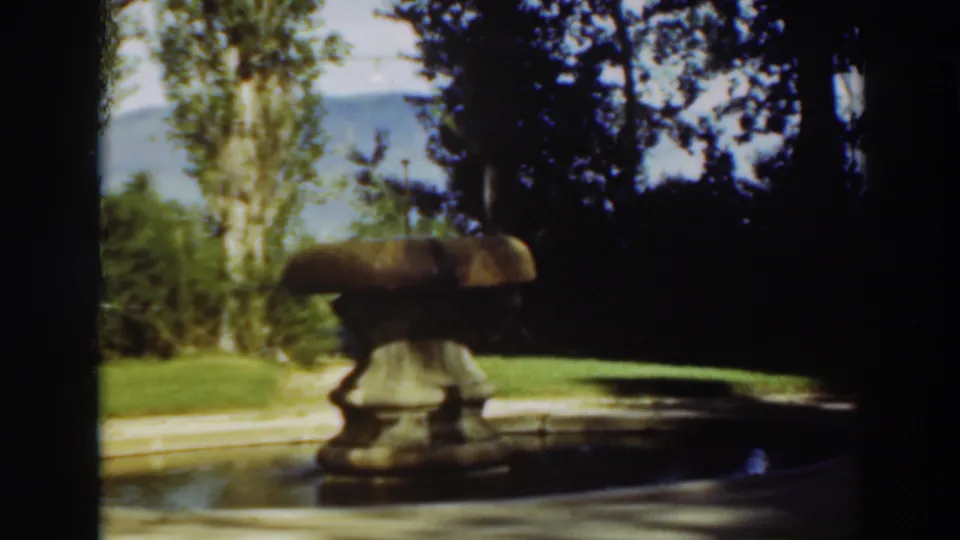 1937 8mm home-movie frame from Virginia City, California, showing a yellow-toned stone fountain near a shaded reflection pool.