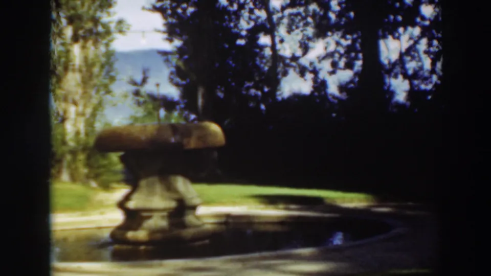 The fountain remains centered in a Virginia City garden view, with the pool edge, lawn, trees, and mountain backdrop visible.