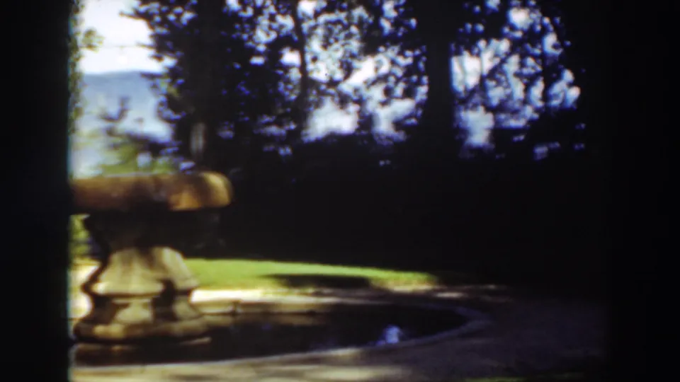 A later frame crops the fountain at left while preserving the shaded pool, green lawn, trees, and hills in the background.