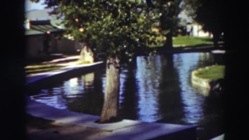 1937 Virginia City, California home-movie still showing a foreground tree beside a curved concrete pool edge and green lawn.