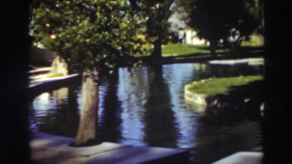 1937 Virginia City, California frame showing a landscaped pool, grass bank, tree shade, walkway, and low buildings in the distance.