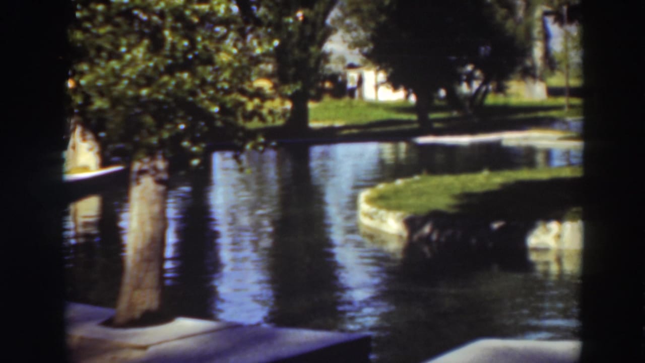 Reflective pond beside a grassy island with trees and stone edging.