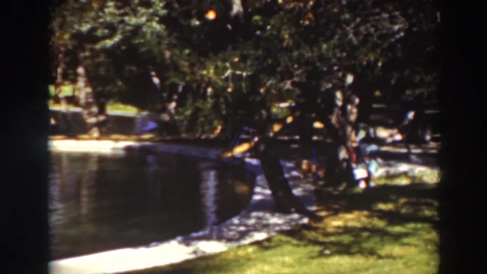 End frame of a 1937 8mm pond view in Virginia City, California, showing shaded water, grass, trees, and a small figure at right.