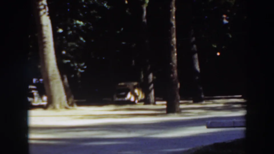 Tree-lined Virginia City, California park or roadside scene from 1937 8mm footage, with a parked car partly visible at left.
