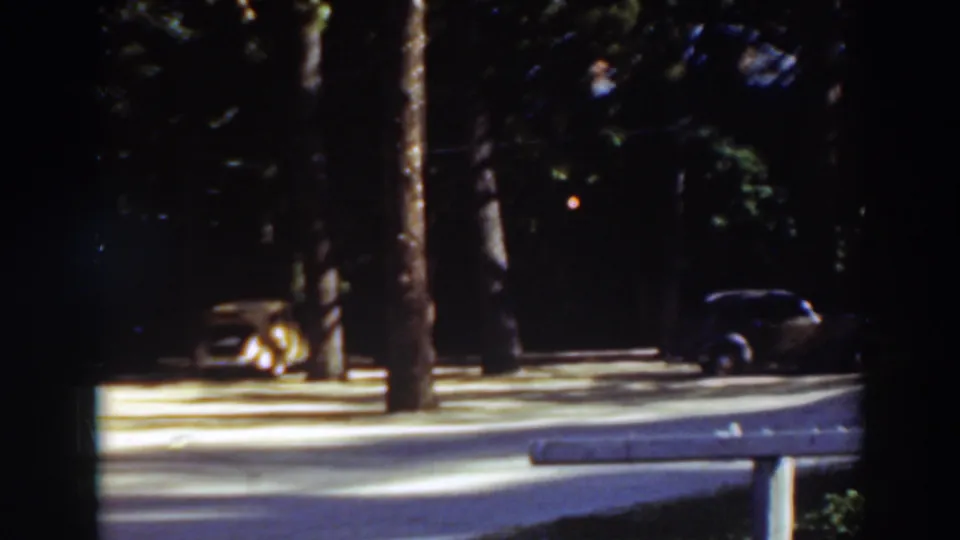 Late-frame view of the 1937 Virginia City, California park scene, showing trees, a parked dark car, and a low roadside rail.