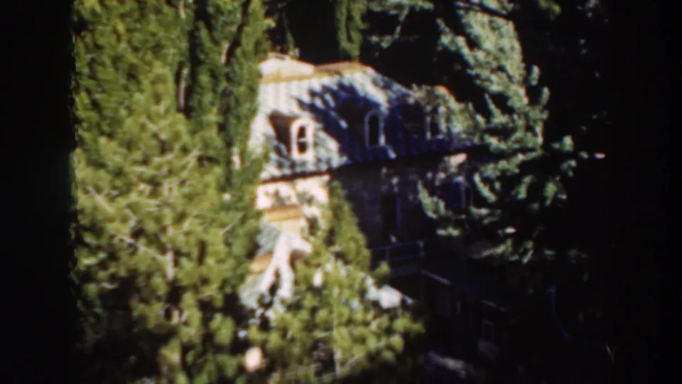 Distant Virginia City house exterior framed by tall trees, with strong sun and shadow across the roofline.
