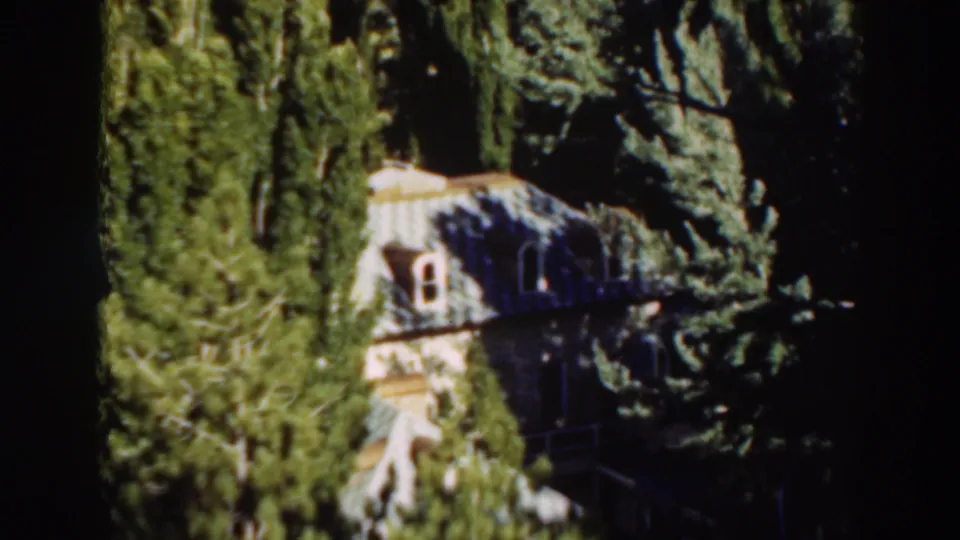 1930s 8mm view of a pale house in Virginia City, California, partly screened by trees and shrubs.