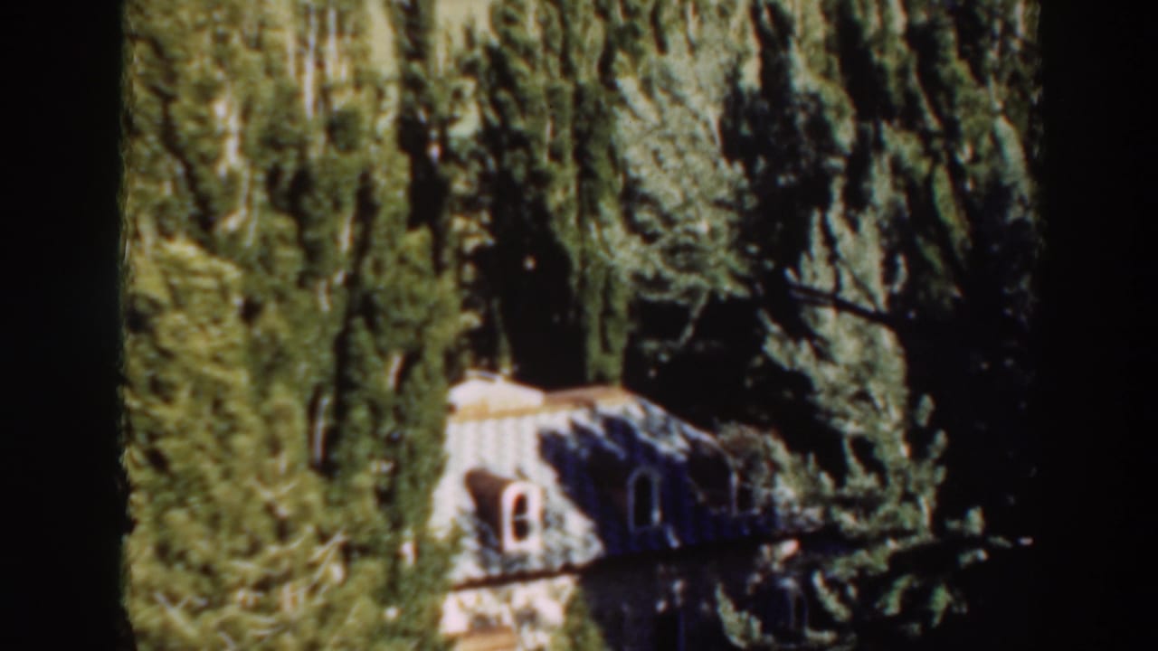 1937 8mm frame from Virginia City, California, showing a house partly hidden among tall trees.