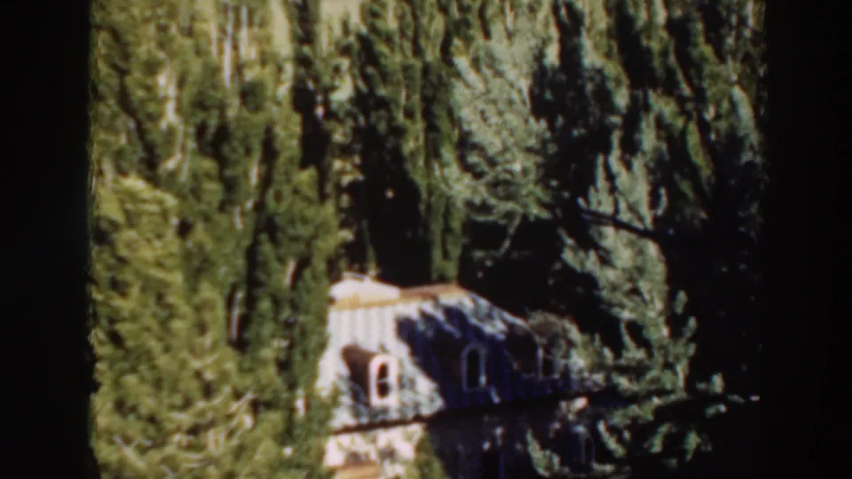 1937 8mm frame from Virginia City, California, showing a house partly hidden among tall trees.