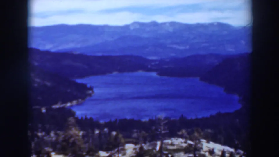 1937 8mm home-movie frame with a high view over a blue mountain lake and dark tree-covered ridges in the stated California location.