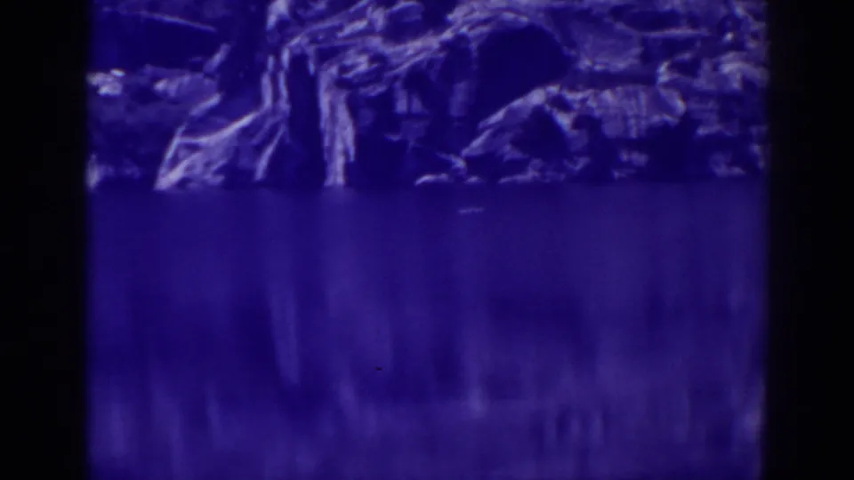 Late-1930s Angora Lakes home-movie view of shoreline rock mirrored in still water.