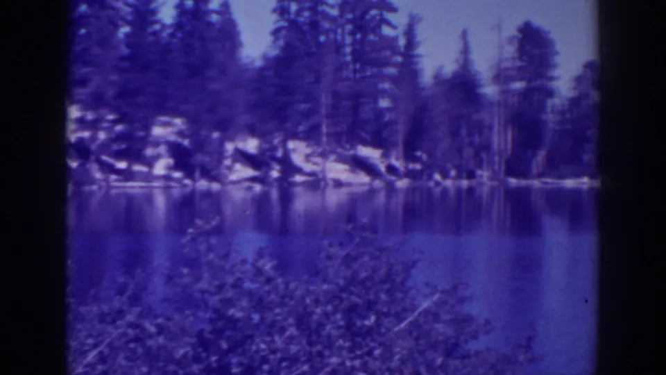 Angora Lakes, California, in a blue-shifted 8mm frame with shrubs, reflective water, rocks, and conifers.