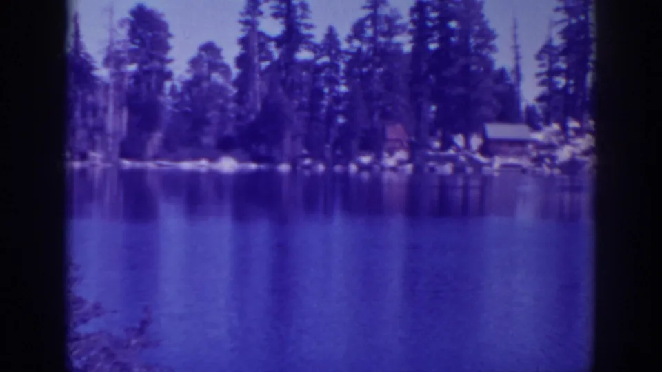 1938 Angora Lakes shoreline with tall pines, small cabins, rocks, and reflections across the water.