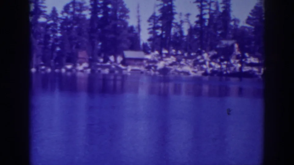 1938 8mm view of Angora Lakes with still blue water, pine trees, rocks and small shoreline cabins.