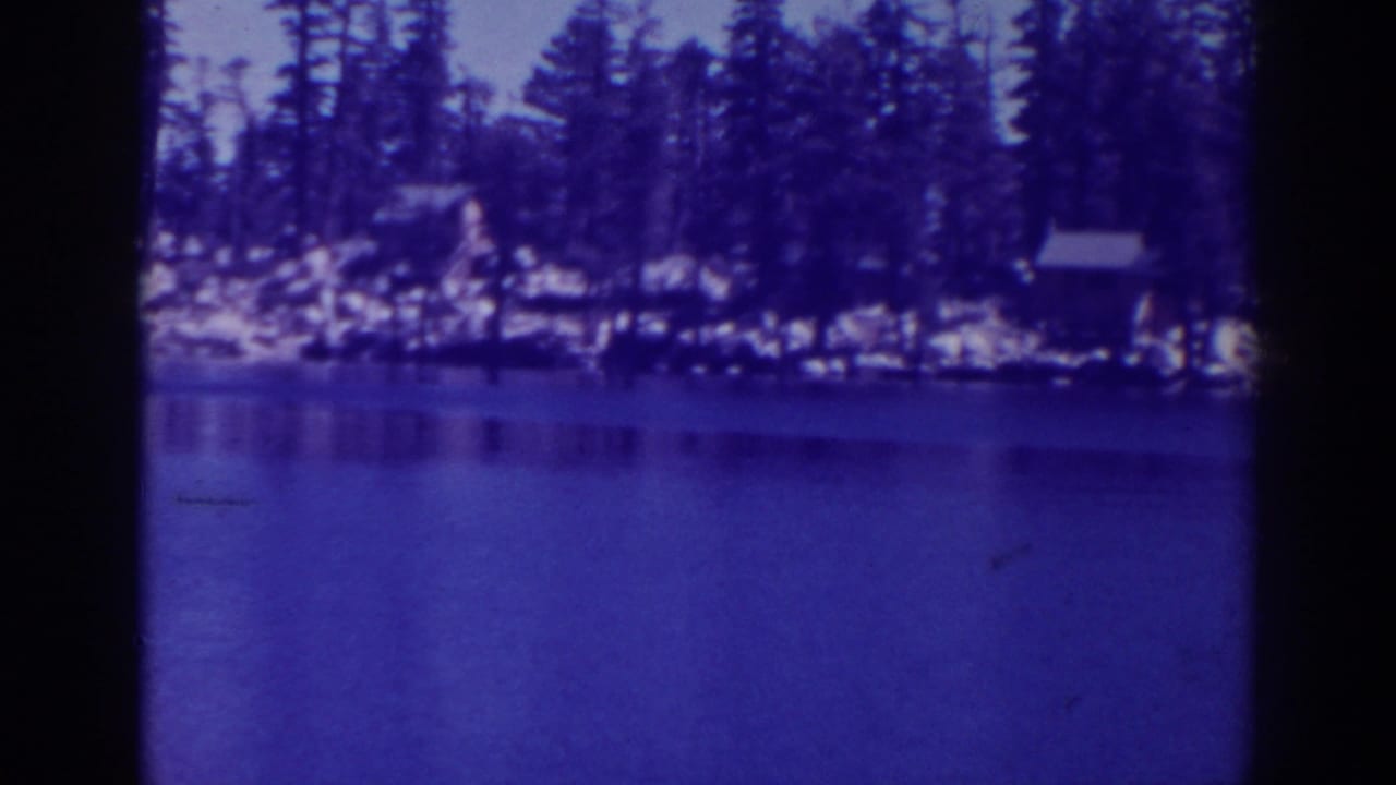 Lower Angora Lake in California, shown in 1938 8mm footage with blue water, pine trees, rocks, and small cabins along the far shore.