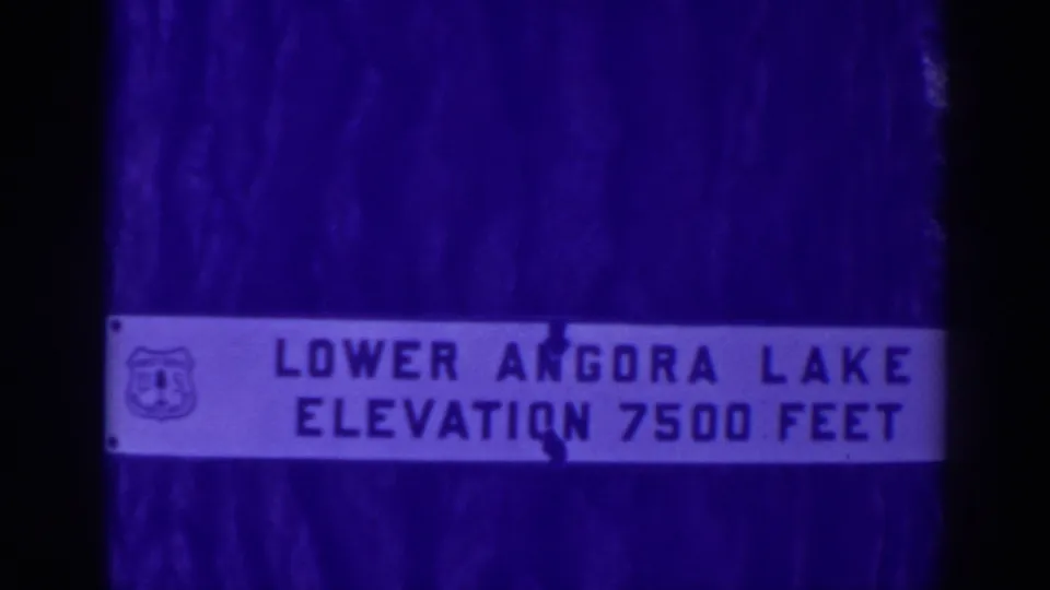 Close view of a U.S. Forest Service-style sign identifying Lower Angora Lake at elevation 7500 feet, filmed in blue-tinted 8mm.
