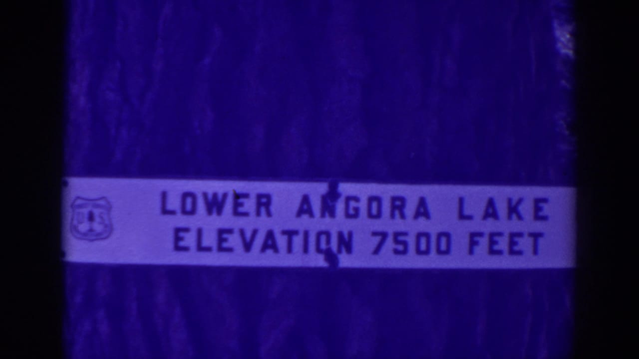Close view of a Lower Angora Lake sign with elevation 7500 feet, framed by dark 8mm film edges and a purple color cast.