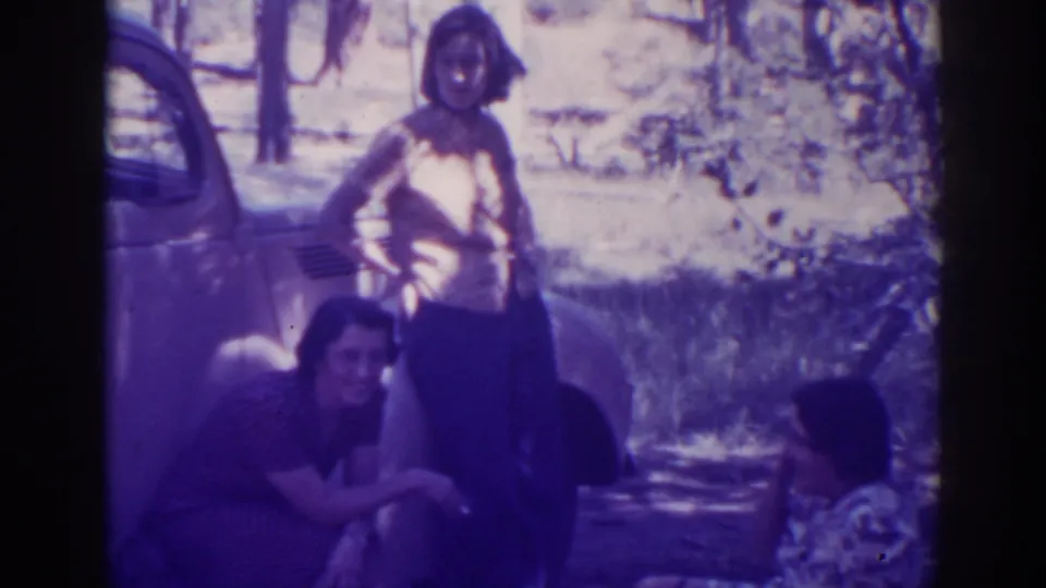 Three women remain near the side of a parked car at Angora Lakes, seen in soft, purple-tinted 8mm home-movie footage.