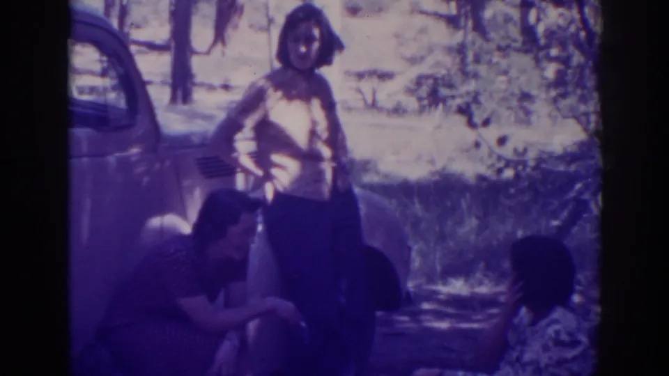 Late shot of three women gathered by a vintage car in the Angora Lakes wooded area, with heavy film borders and soft exposure.