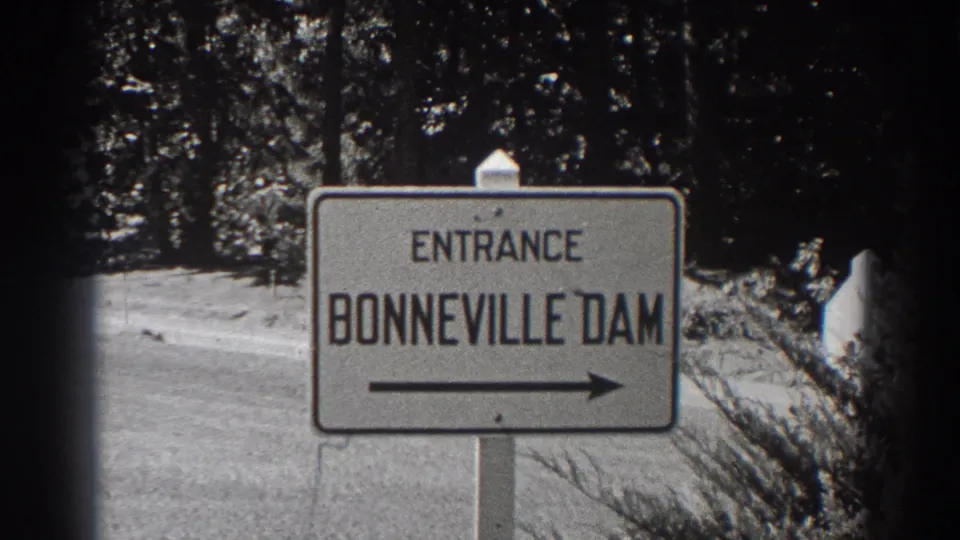 Visitor-shot 8mm frame of the Bonneville Dam entrance sign, with the arrow pointing along the road.
