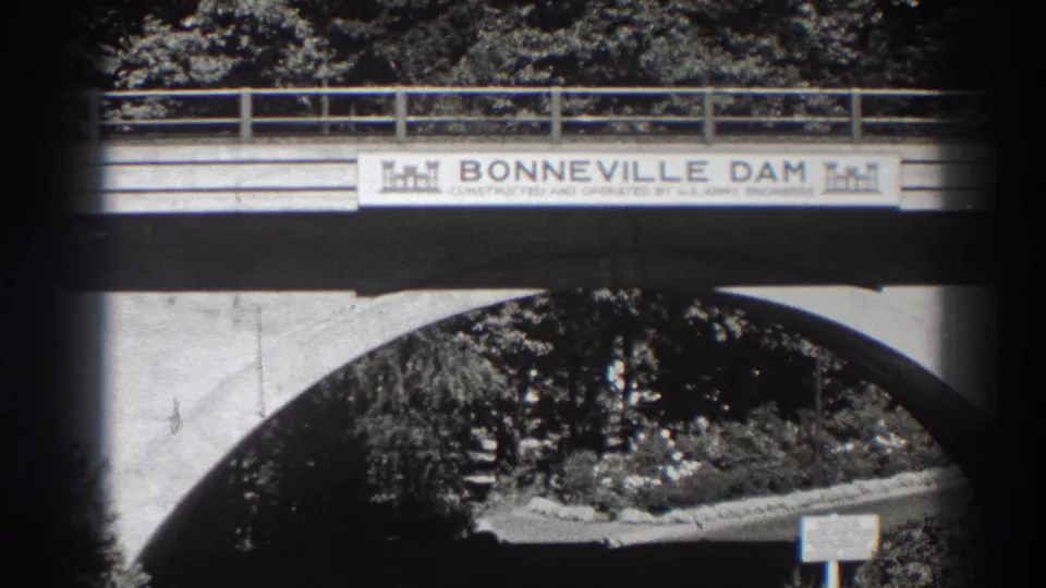 Final 1938 frame holds on the Bonneville Dam bridge banner, with concrete arch geometry, railings, trees, and a small sign below.