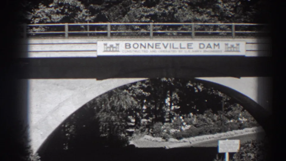 1938 8mm view of the Bonneville Dam entrance sign on a bridge, with a concrete arch, railing, trees, and a small lower sign.