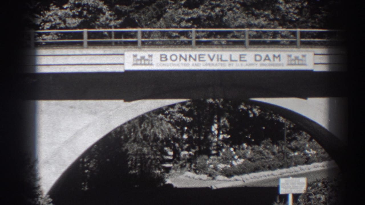 1938 Bonneville Dam bridge view in Oregon, showing the sign, concrete arch, railing, trees, and roadway beneath.