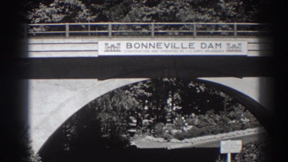 1938 Bonneville Dam bridge view in Oregon, showing the sign, concrete arch, railing, trees, and roadway beneath.